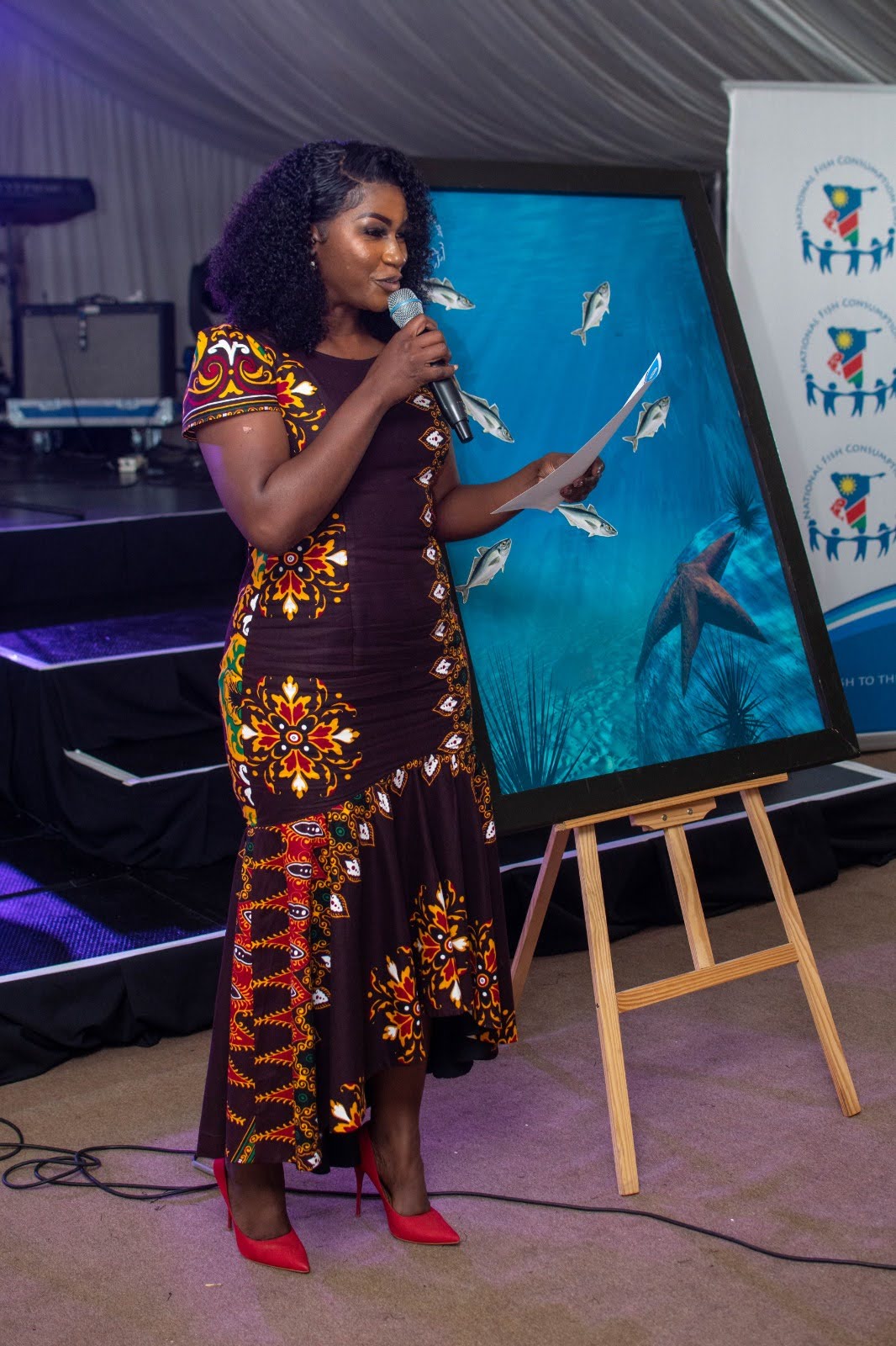 Lorraine Kondombolo presenting beside a commemorative artwork